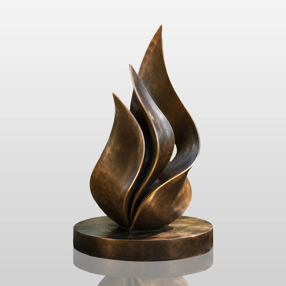 An abstract bronze sculpture sits surrounded by green plants in a sunlit garden.
