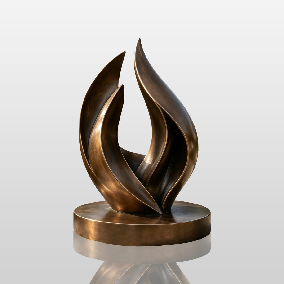 An abstract bronze flame sculpture sits on the stone paving in a lush green garden.