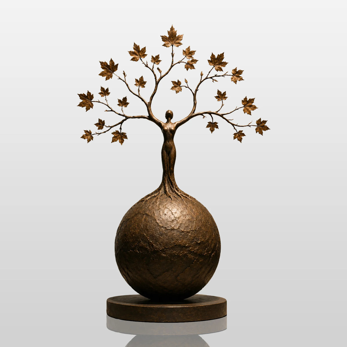 Bronze tree woman sphere sculpture rests on an indoor display surface against a neutral wall.