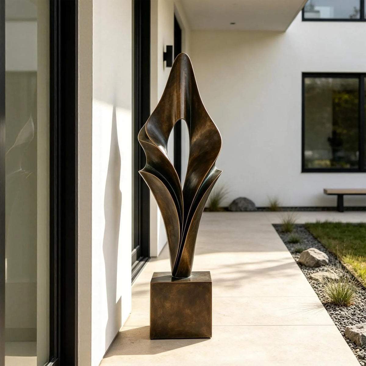 An abstract folded bronze sculpture stands on the entry walkway of a modern home.