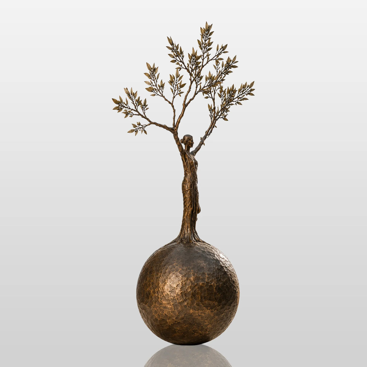 Bronze sculpture with the design of human shaped tree ball stands in a cobblestone courtyard.