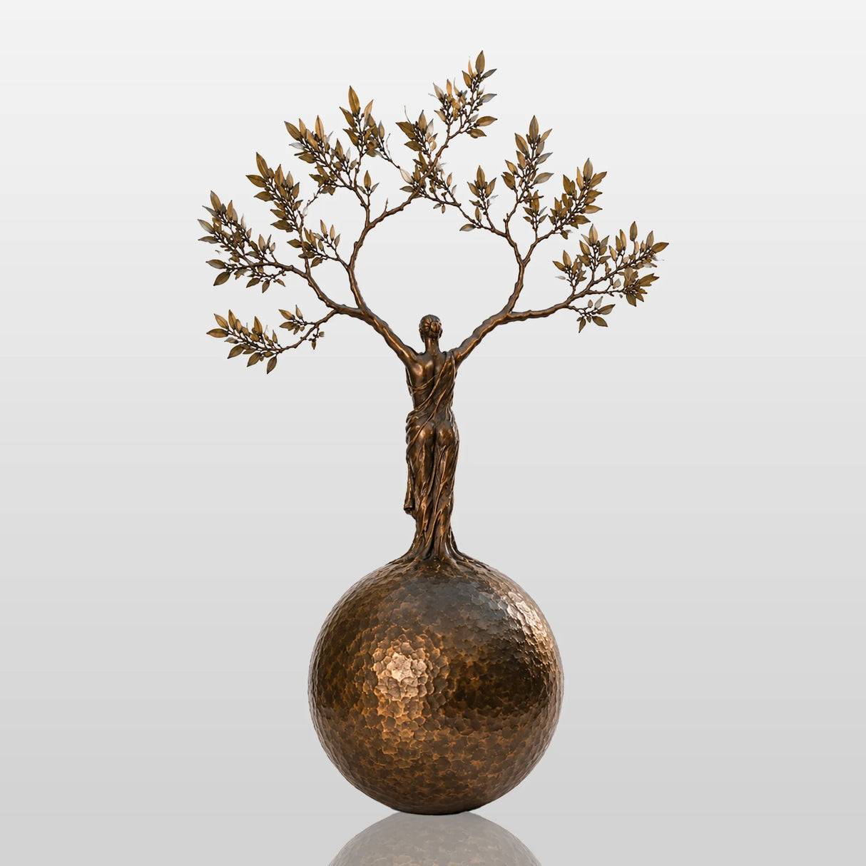 Bronze sculpture with the design of human shaped tree ball stands in a cobblestone courtyard.