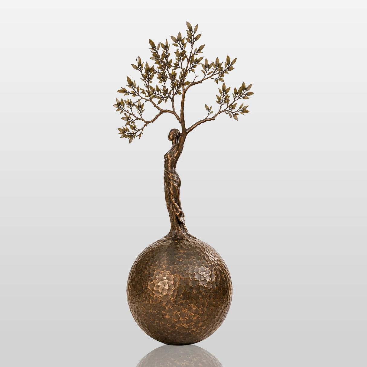 Bronze sculpture with the design of human shaped tree ball stands in a cobblestone courtyard.