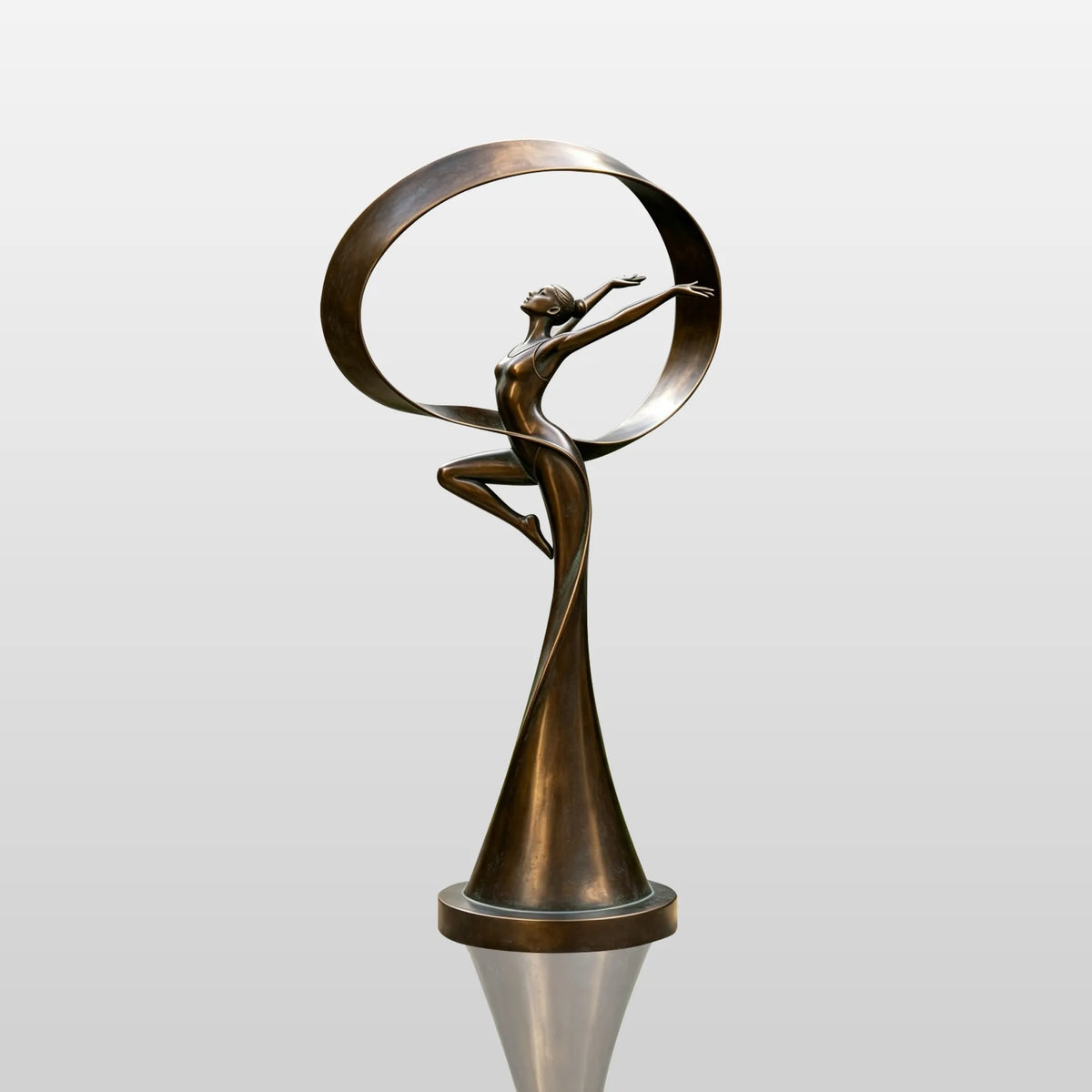 The bronze dancer sculpture with a ribbon sits on gravel beside green lawn.