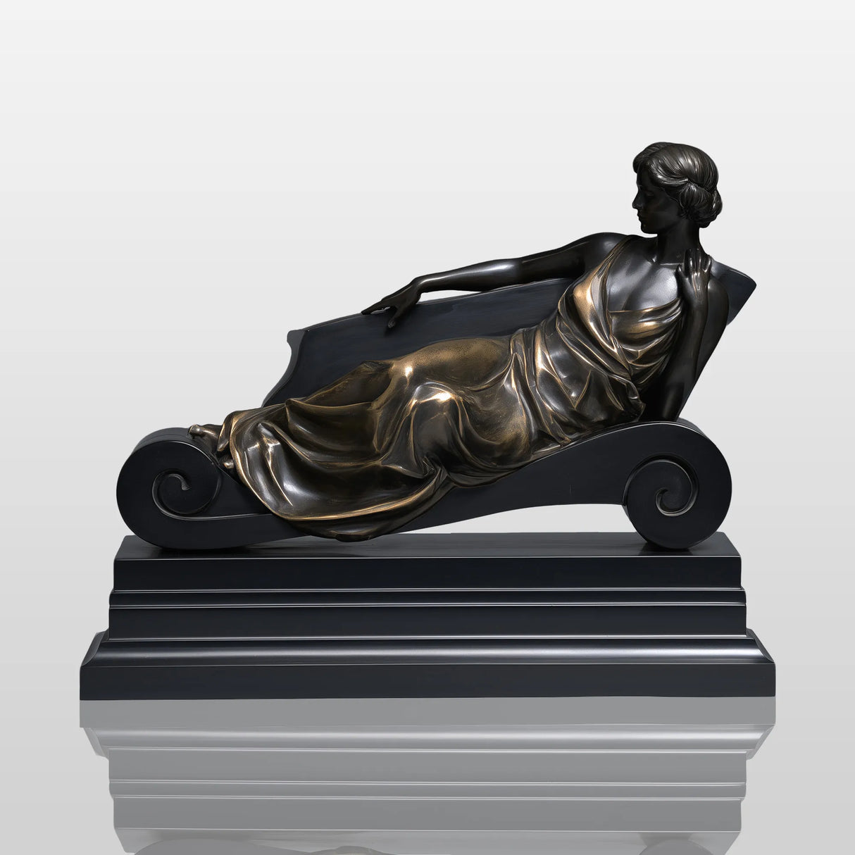 Bronze reclining lady table sculpture sits on light indoor table beside vintage books and table lamp.