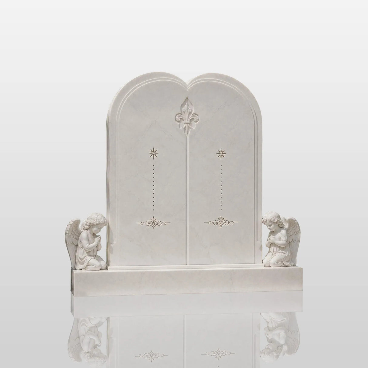 White double marble heart tombstone flanked by two praying angel statues sits in a quiet green memorial garden.