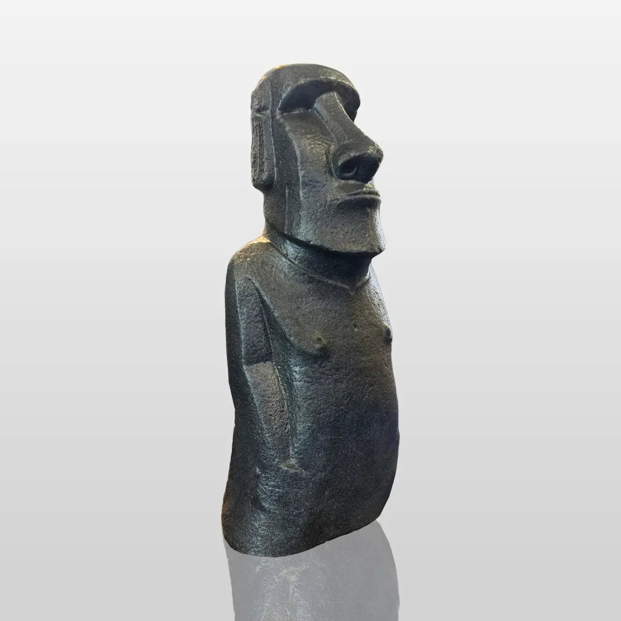 A large textured Moai stone statue rests surrounded by natural rocks inside a minimalist art gallery lit by ceiling spotlights.