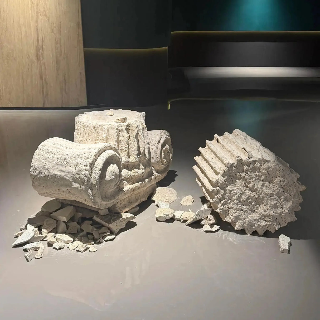 A set of Ionic column marble sculptures rests on a smooth display table with scattered stone fragments around them.