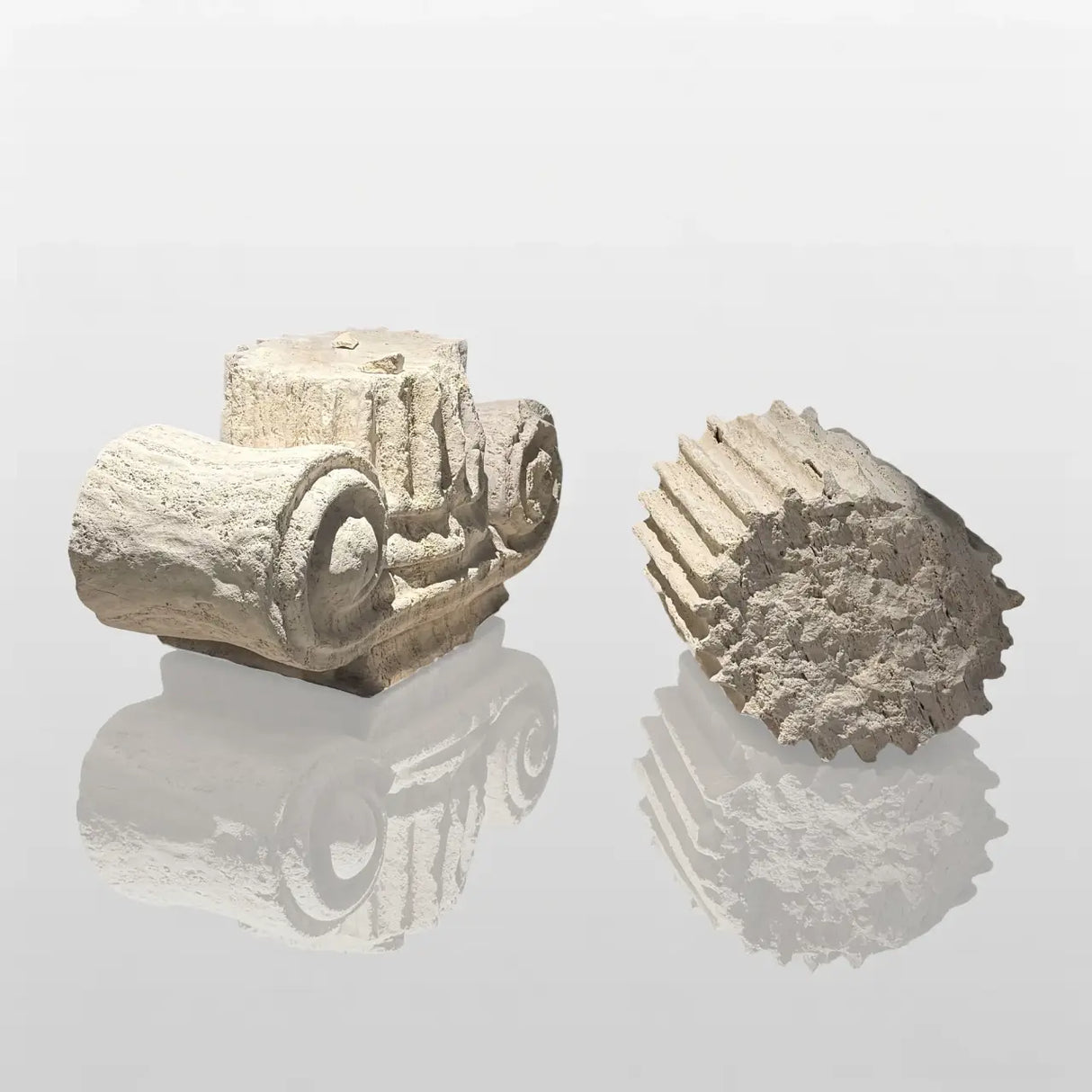 A set of Ionic column marble sculptures rests on a smooth display table with scattered stone fragments around them.