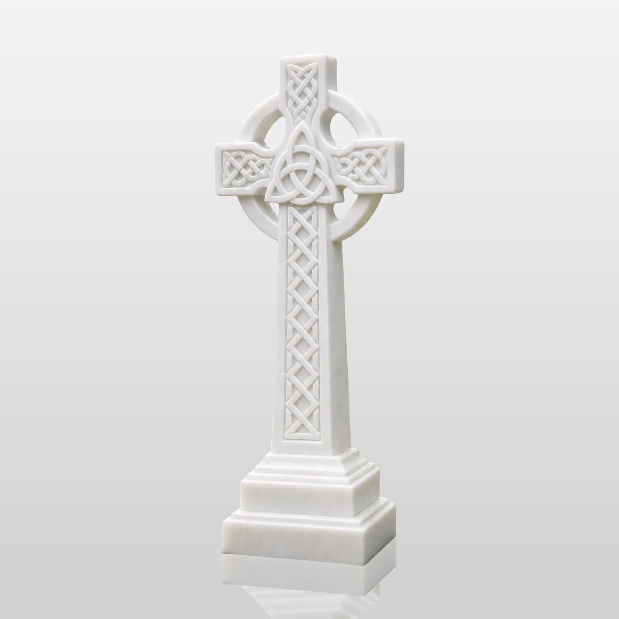 White marble Celtic cross tombstone stands on gravel ground surrounded by green plants.