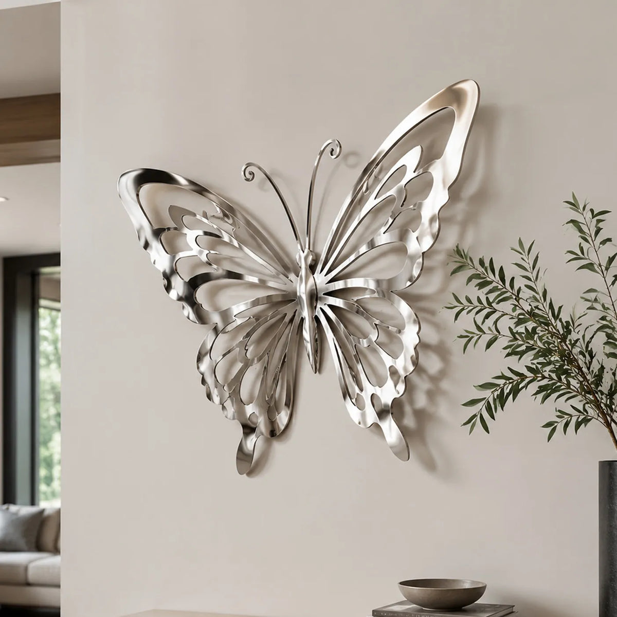 A shiny stainless steel butterfly wall sculpture is mounted on a plain white interior wall.