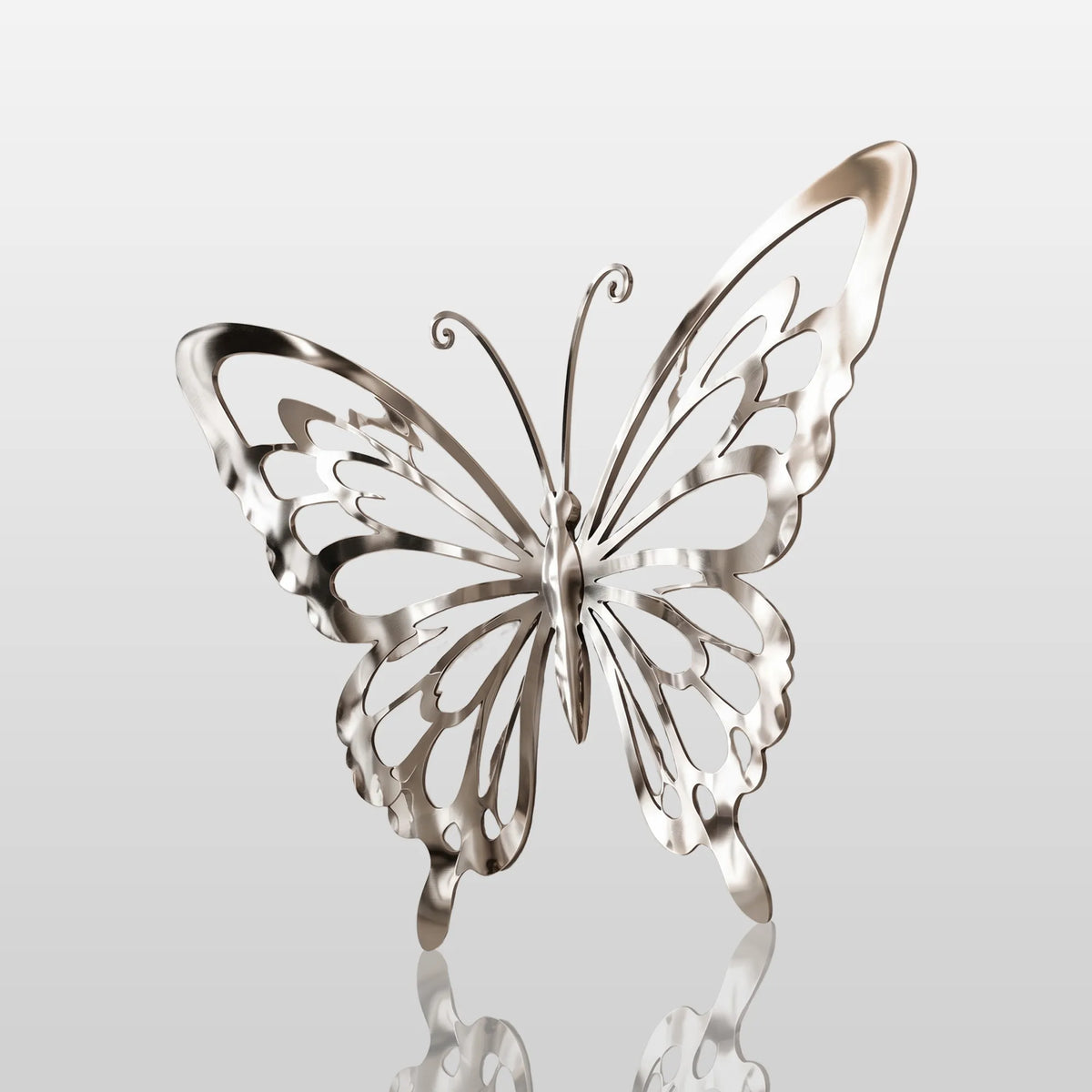 A shiny stainless steel butterfly wall sculpture is mounted on a plain white interior wall.