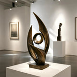 An abstract bronze sculpture rests on a white pedestal inside an art gallery.