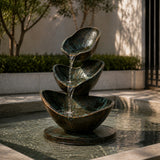 Three tier bronze fountain pours flowing water in an outdoor garden.