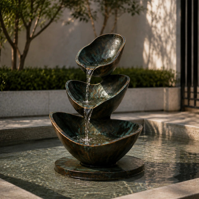 Three tier bronze fountain pours flowing water in an outdoor garden.