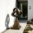 This bronze loop sculpture stands on paved walkway outside a modern house.