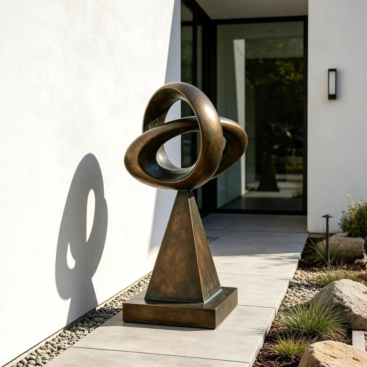 This bronze loop sculpture stands on paved walkway outside a modern house.