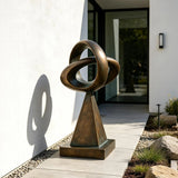 This bronze loop sculpture stands on paved walkway outside a modern house.