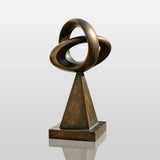 This bronze loop sculpture stands on paved walkway outside a modern house.