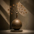 Bronze tree woman sphere sculpture rests on an indoor display surface against a neutral wall.