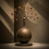 Bronze tree woman sphere sculpture rests on an indoor display surface against a neutral wall.