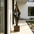An abstract folded bronze sculpture stands on the entry walkway of a modern home.