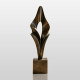 An abstract folded bronze sculpture stands on the entry walkway of a modern home.