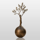 Bronze sculpture with the design of human shaped tree ball stands in a cobblestone courtyard.