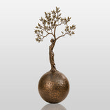 Bronze sculpture with the design of human shaped tree ball stands in a cobblestone courtyard.