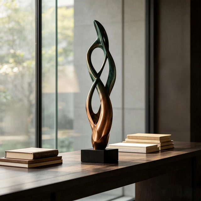 Abstract bronze table sculpture sits on the wooden table beside stacked books.