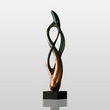 Abstract bronze table sculpture sits on the wooden table beside stacked books.