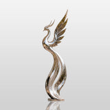 A polished abstract stainless steel phoenix sculpture stands on a stone pedestal at the front entry of a light colored villa beside trimmed topiary shrubs.