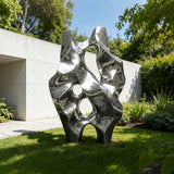 An abstract stainless steel sculpture stands on green grass beside a modern building.