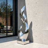 Mirror polished stainless steel twisted sculpture stands by a modern building.