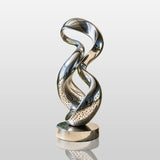 Stainless steel twisted loop sculpture stands on the outdoor patio beside a modern building.