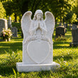 Marble tombstone carved with praying angel, roses and heart stands on the lush green cemetery lawn.
