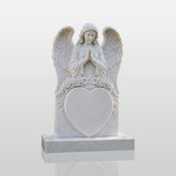 Marble tombstone carved with praying angel, roses and heart stands on the lush green cemetery lawn.