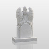 Marble tombstone carved with praying angel, roses and heart stands on the lush green cemetery lawn.