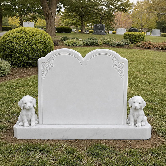 A white marble tombstone with two puppy statues stands on green grass inside a cemetery.