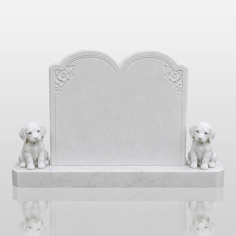 A white marble tombstone with two puppy statues stands on green grass inside a cemetery.