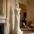 A white marble female statue stands gracefully in an elegant classical interior with warm curved details.