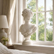 Marble blindfolded lady bust stands on a bright bedroom windowsill.