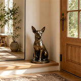 Bronze chihuahua dog statue sits on wooden entryway ledge inside home.