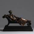 Bronze tabletop sculpture presents a semi nude lady, reclining on studded scroll chaise lounge with multi layer black base.