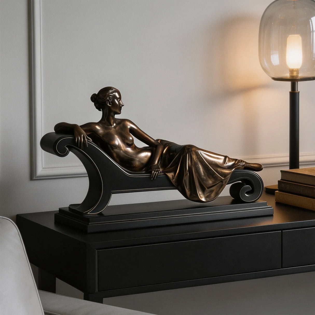 Bronze tabletop reclining lady sculpture is displayed on black cabinet within modern styled interior space.