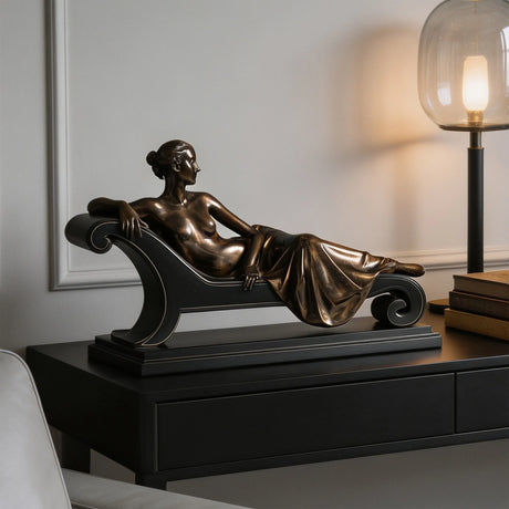 Bronze tabletop reclining lady sculpture is displayed on black cabinet within modern styled interior space.