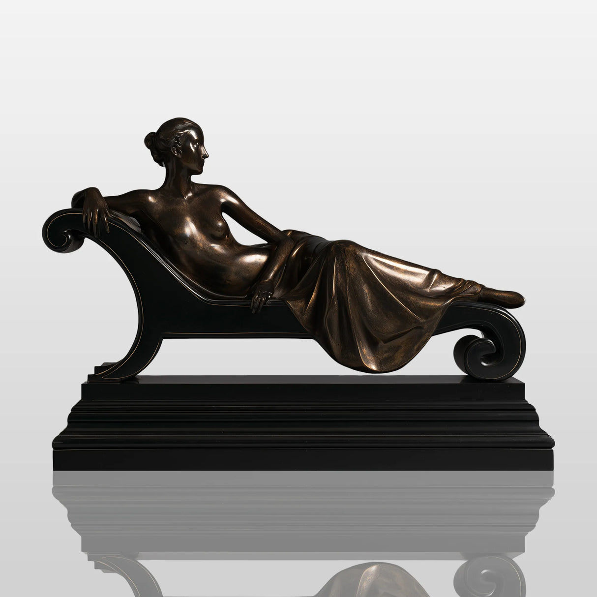 Bronze tabletop reclining lady sculpture is displayed on black cabinet within modern styled interior space.