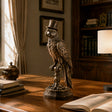 Antique bronze parrot sculpture rests on a study desk beside stacked books and open reading volume.