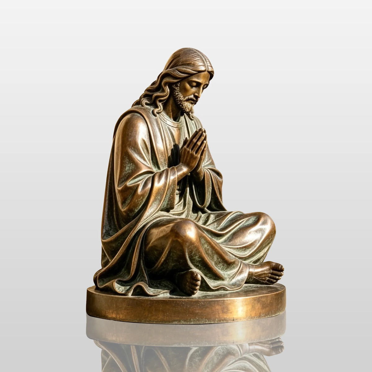 A bronze seated praying Jesus statue sits on stone step outside a church.