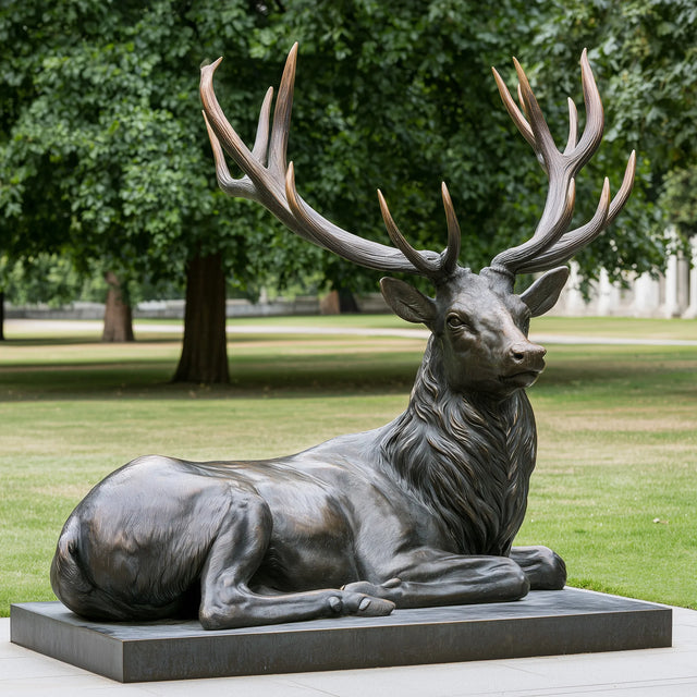 Bronze deer statue rests on a flat base within a lush green park.